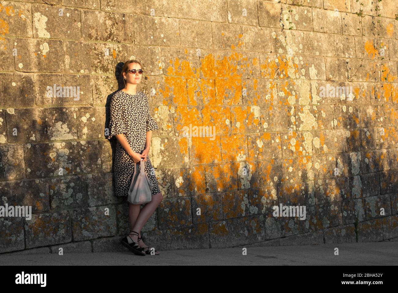 Woman leaning against overgrown wall in the evening sun Stock Photo