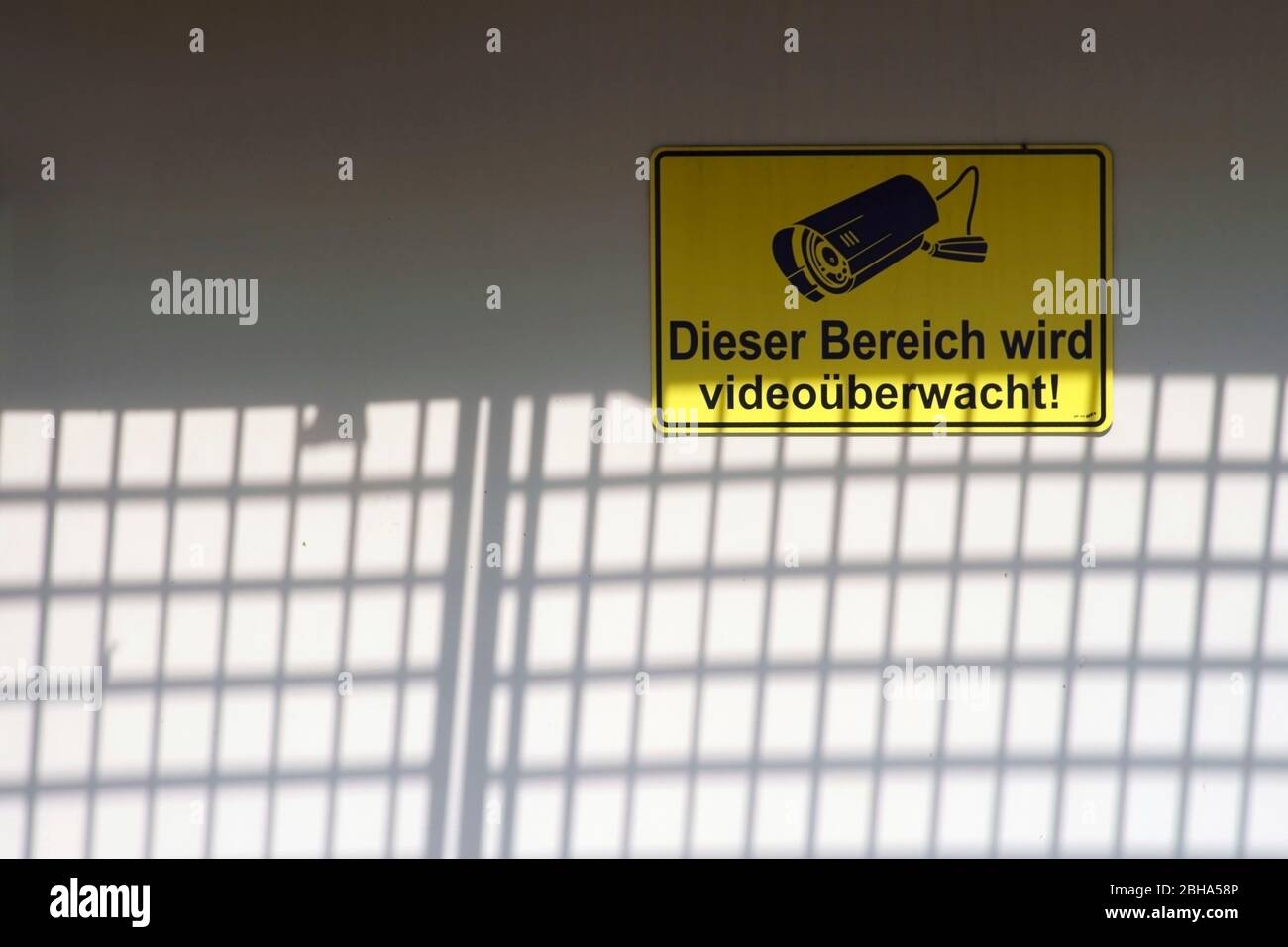 A yellow video security sign behind a fence casting shadows. Stock Photo