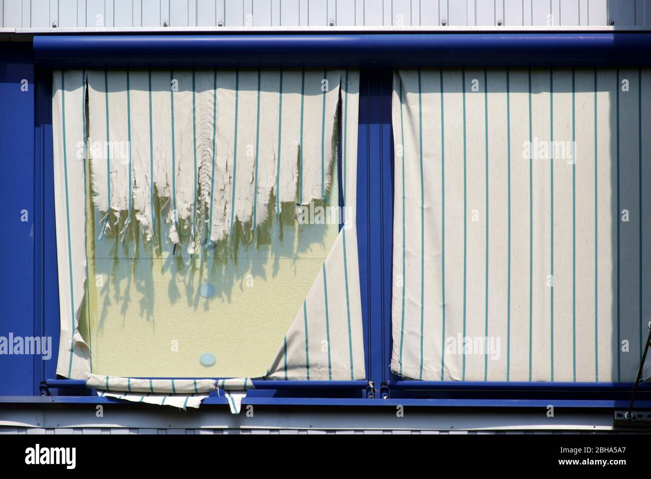 Torn fabric drapes on the windows of an upper floor of a commercial building. Stock Photo