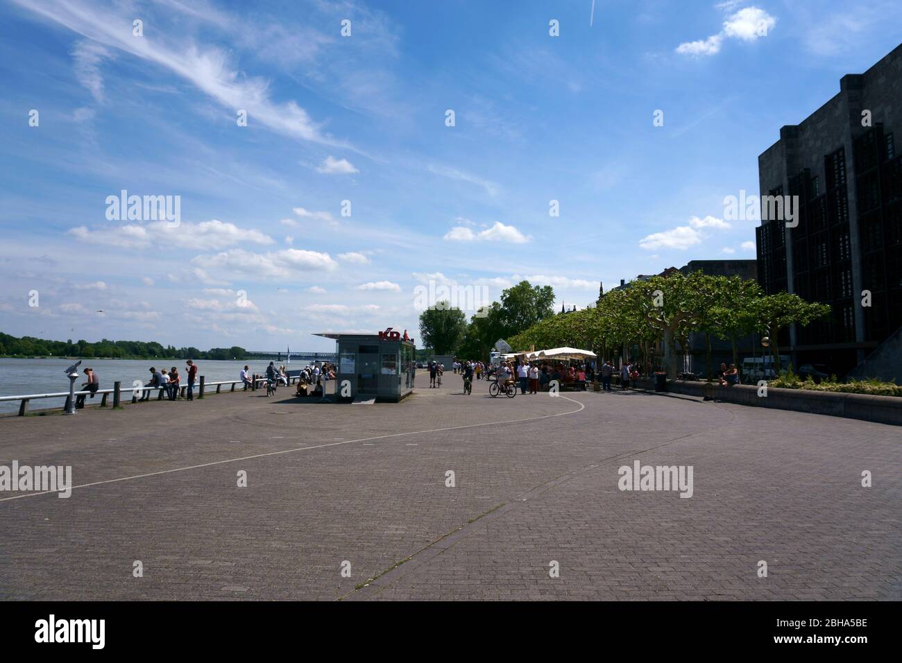 People walk along the waterfront of the Rhine in Mainz behind the town hall in fine weather. Stock Photo