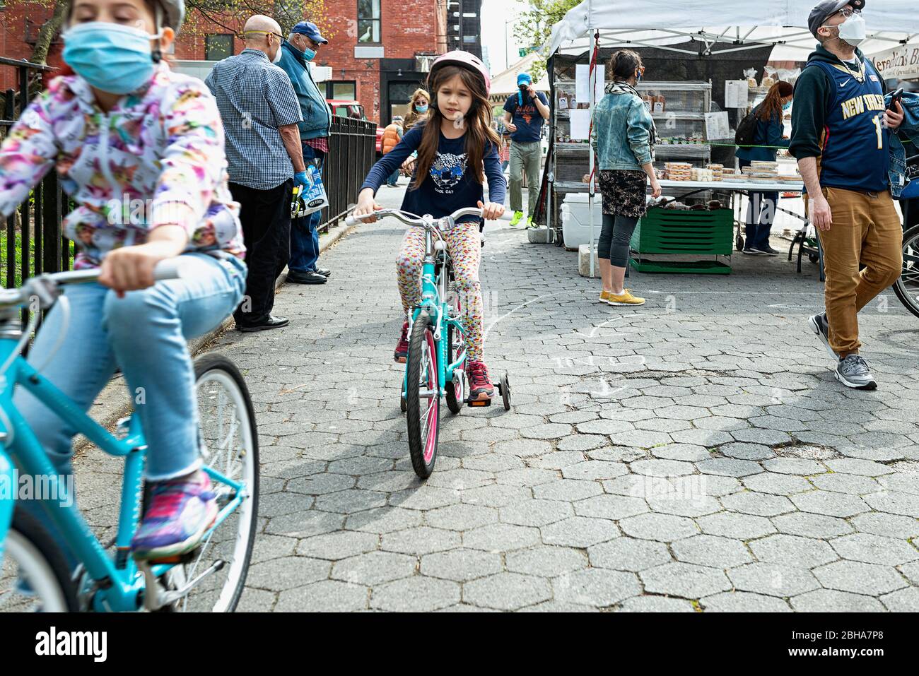 Kids riding bicycles through a farmers market in New York City during the COVID 19 pandemic in New York City in April 2020 Stock Photo