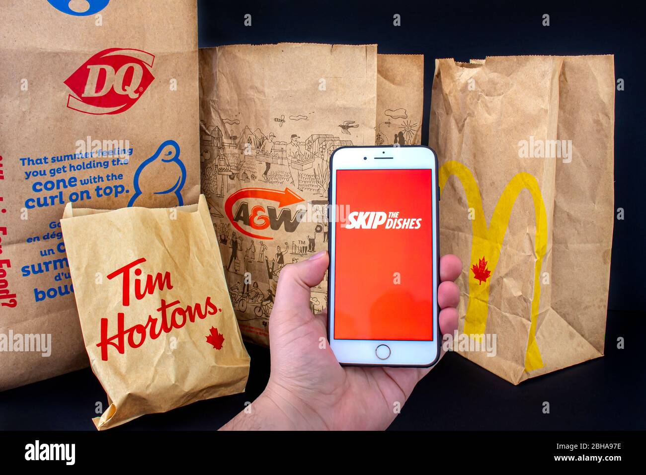 Calgary, Alberta. Canada. April 24, 2020: A person holding an iPhone Plus with the Skip the dishes application open with delivered food bags from Tim Stock Photo