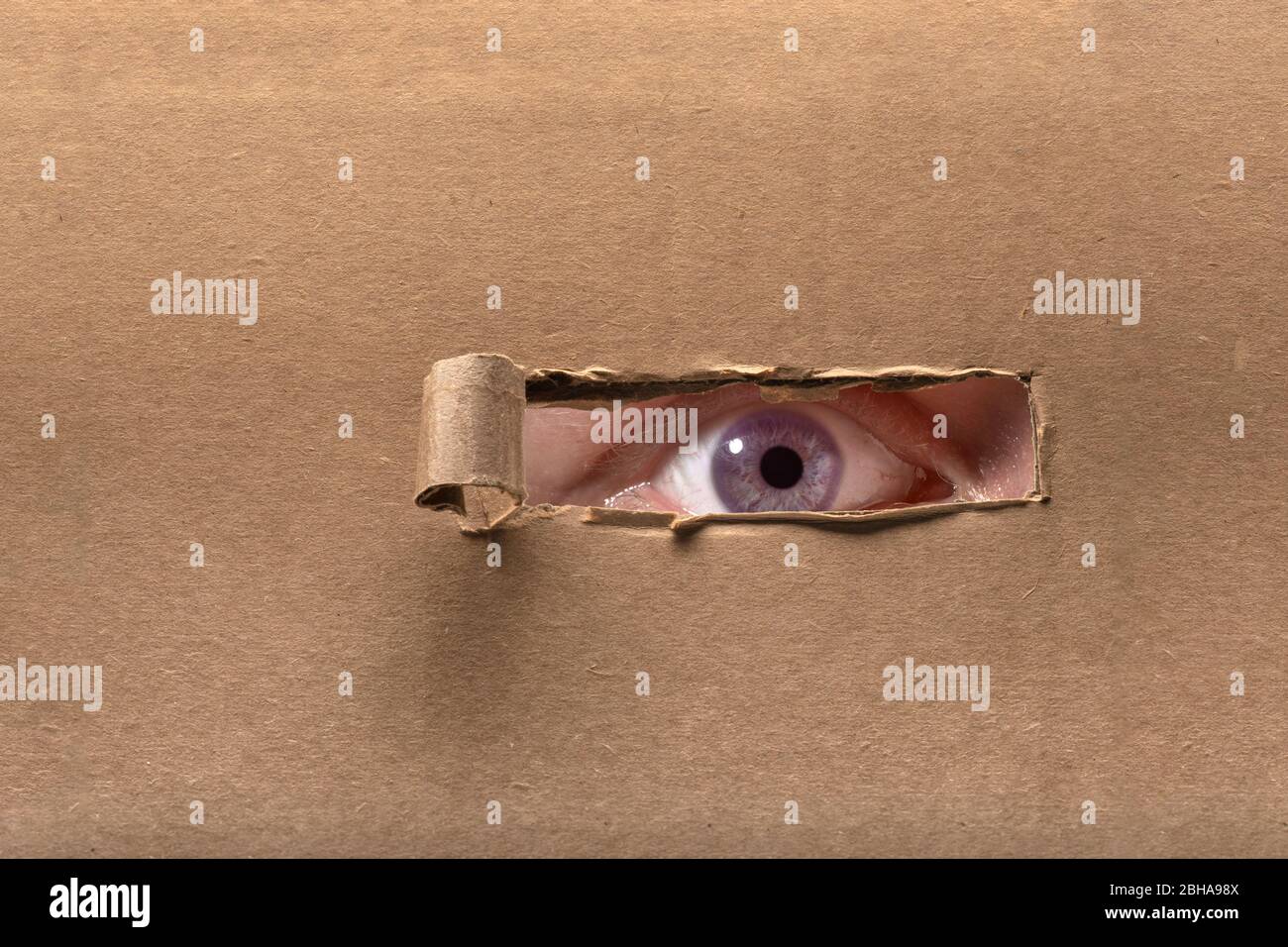 Eye peeking through torn paper Stock Photo