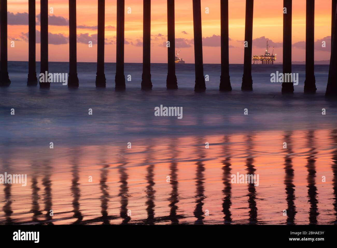 Oil rigs behind columns of Huntington Beach Pier at sunset, California, USA Stock Photo