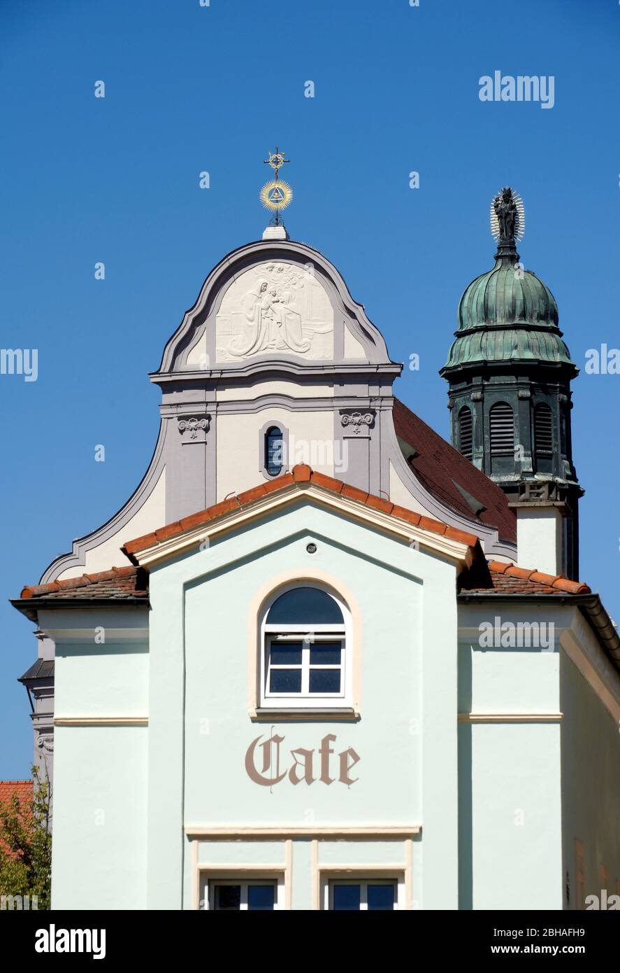 Germany, Bavaria, Upper Bavaria, Altötting, St. Anna's Basilica, church tower with statue of Mary and baby Jesus, front facade with relief image of the patron saint of St. Anne with Mary and baby Jesus, in the foreground a cafe Stock Photo
