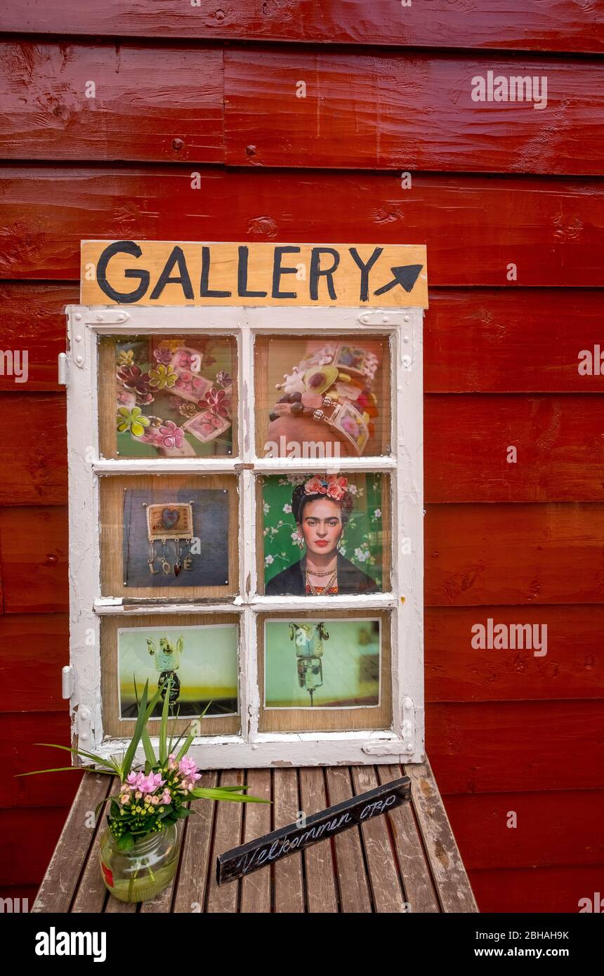 white wooden window on a wooden table with flowers and welcome sign, with fleiled images in front of a red wooden house wall with signs to the Gallery in Bryggen, Bergen, Hordaland, Norway, Scandinavia, Europe Stock Photo