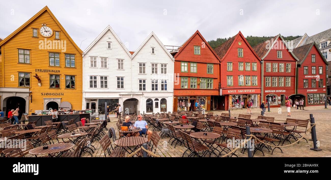 Tourists sit at tables against the historic backdrop of colorful wooden houses in Bryggen in the Hanseatic quarter of Bryggen, Torget, The German Wharf, Bergen, Hordaland, Norway, Scandinavia, Europe Stock Photo