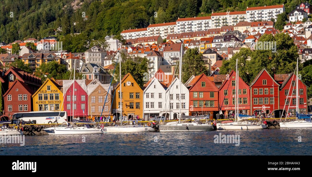 Nordsee, behind a colorful wooden houses front with attached sailboats in the harbor of Bryggen, behind it further houses of the place above hotel complexes and forest-covered mountains, mountains, Hordaland, Norway, Scandinavia, Europe Stock Photo
