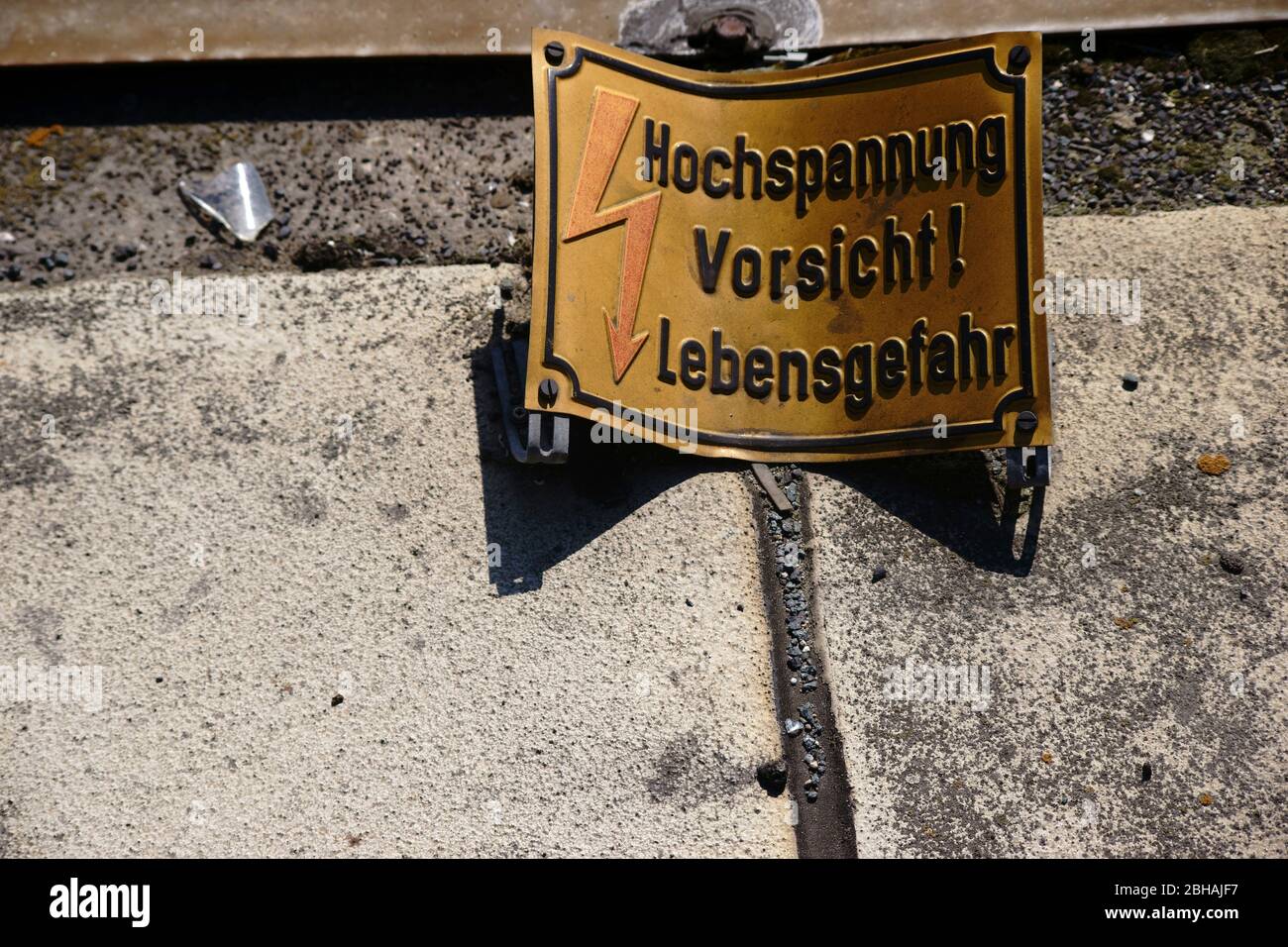A dented and rusted warning sign with the note: Caution high voltage. Stock Photo