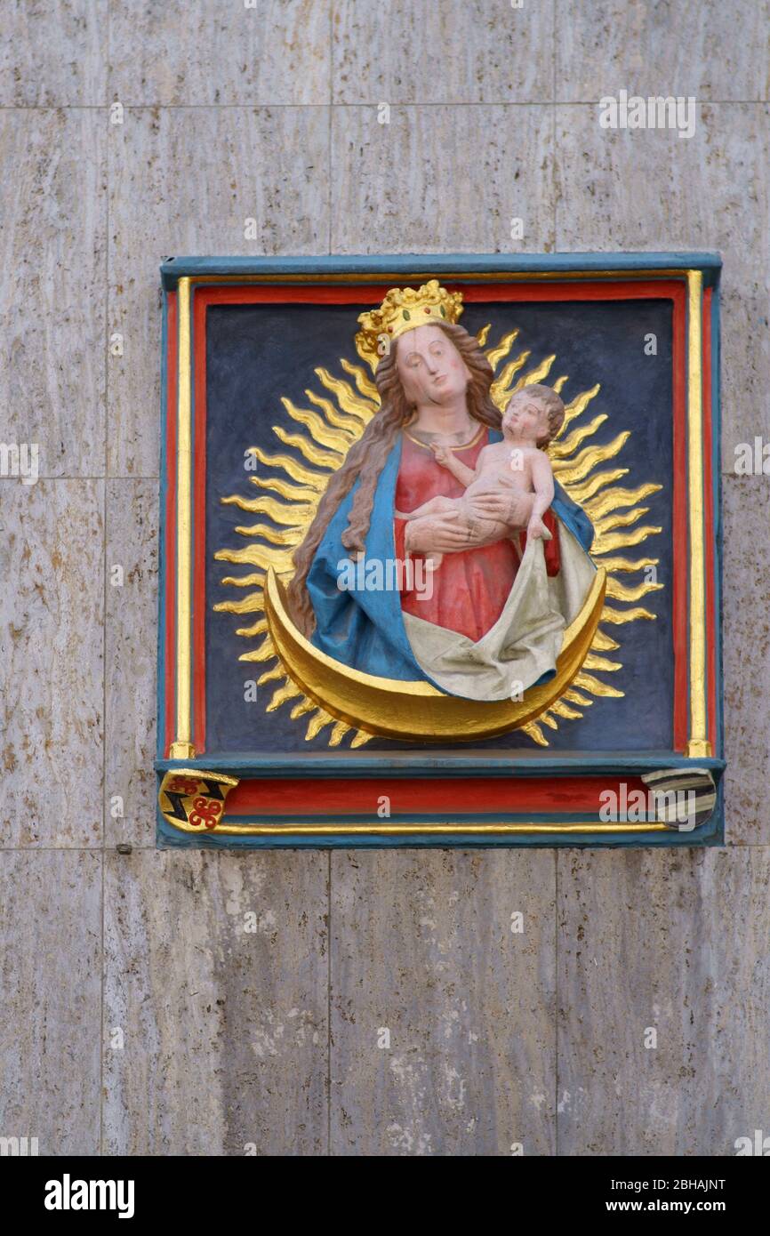 The gilded relief of Mother Mary with the baby Jesus and a radiate wreath on the outer facade of a building in the cathedral street in Mainz. Stock Photo