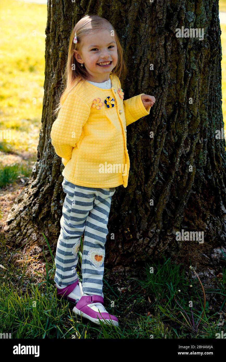little girl leaning against the trunk of an old tree Stock Photo