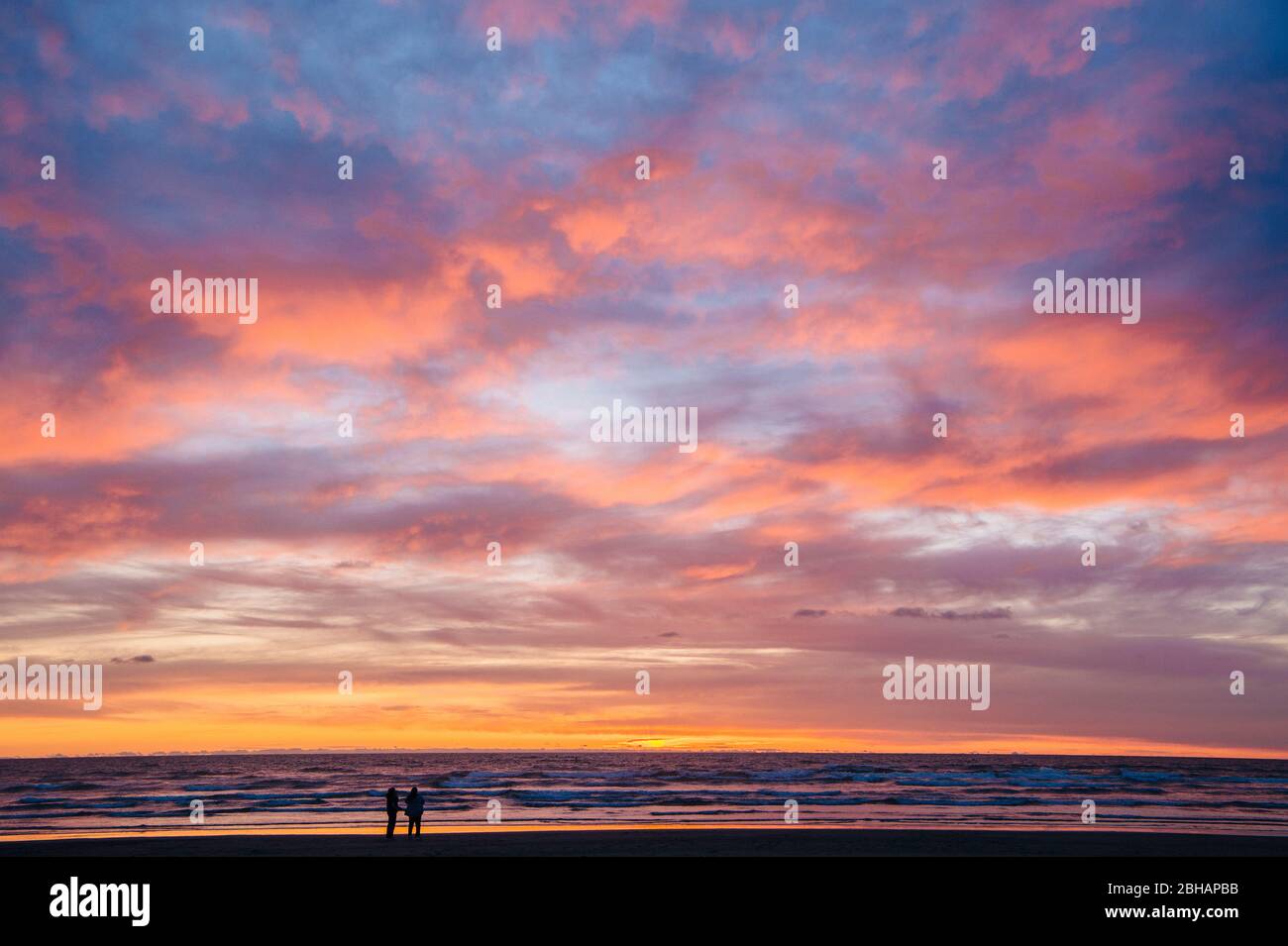 Silhouette of two people standing on beach against dramatic sky at sunset, Seaside, Oregon, USA Stock Photo