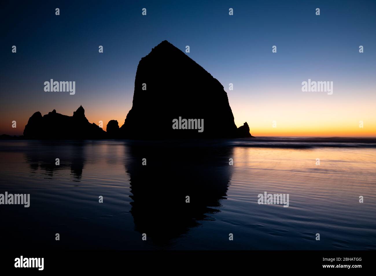 Rock formations reflecting in water at sunset, Cannon Beach, Oregon, USA Stock Photo