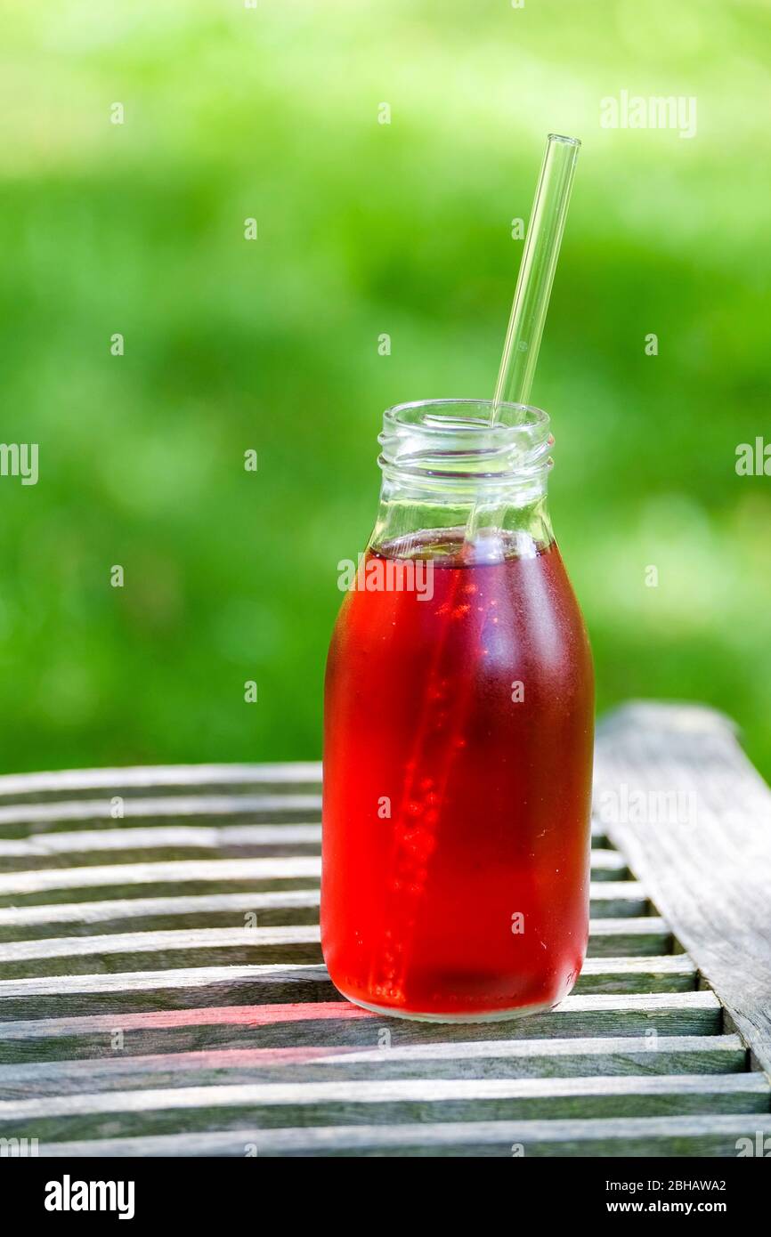 Small bottle with red lemonade on a wooden table in the garden Stock Photo