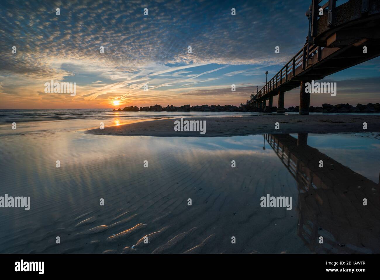 Baltic Sea in the radiant backlight with the pier in Wustrow and reflection of the beautiful clouds on the beach Stock Photo