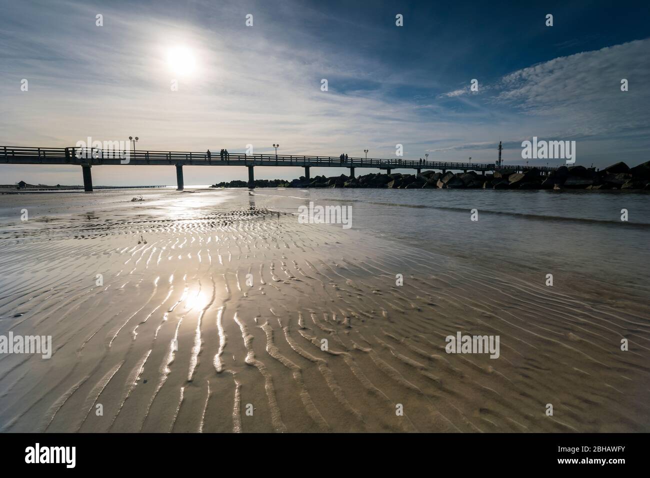 Ostsee im strahlenden Gegenlicht mit der Seebrücke in Wustrow und Spiegelung der schönen Wolken am Strand Stock Photo