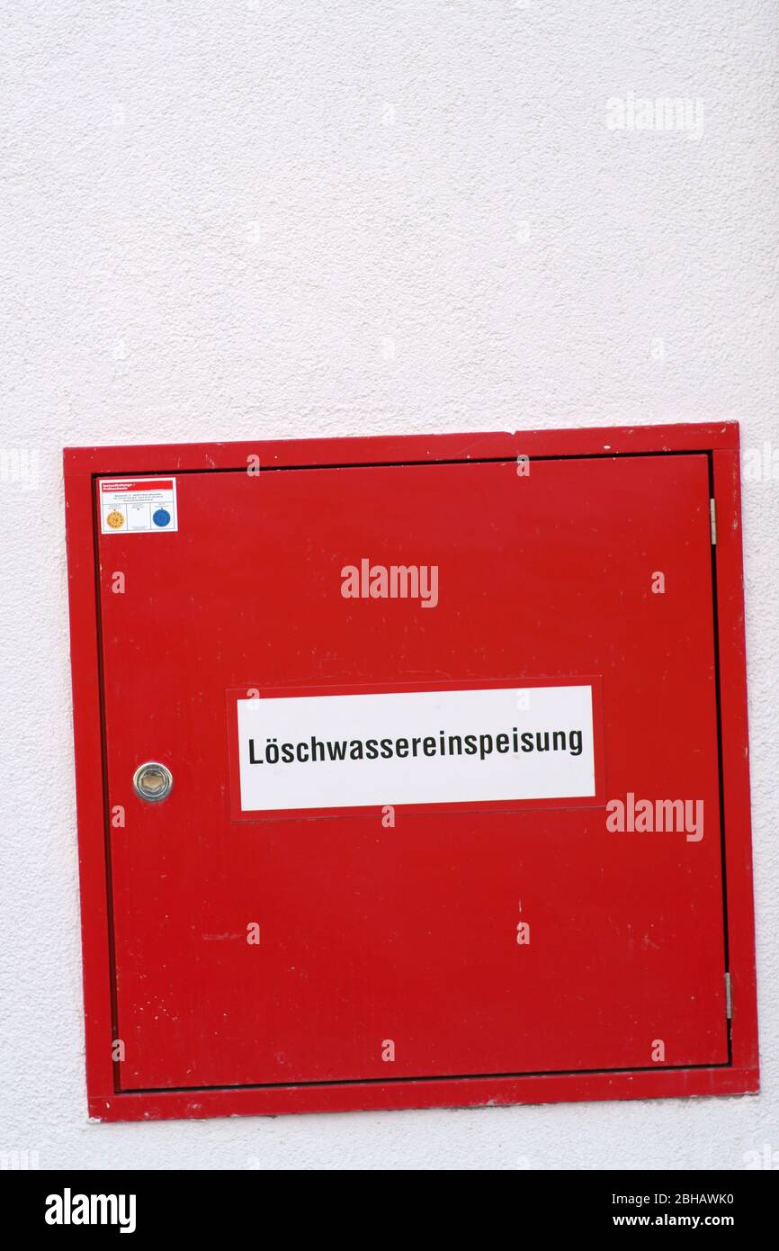 An extinguishing water feed installed in the wall behind a metal door with red signal color. Stock Photo