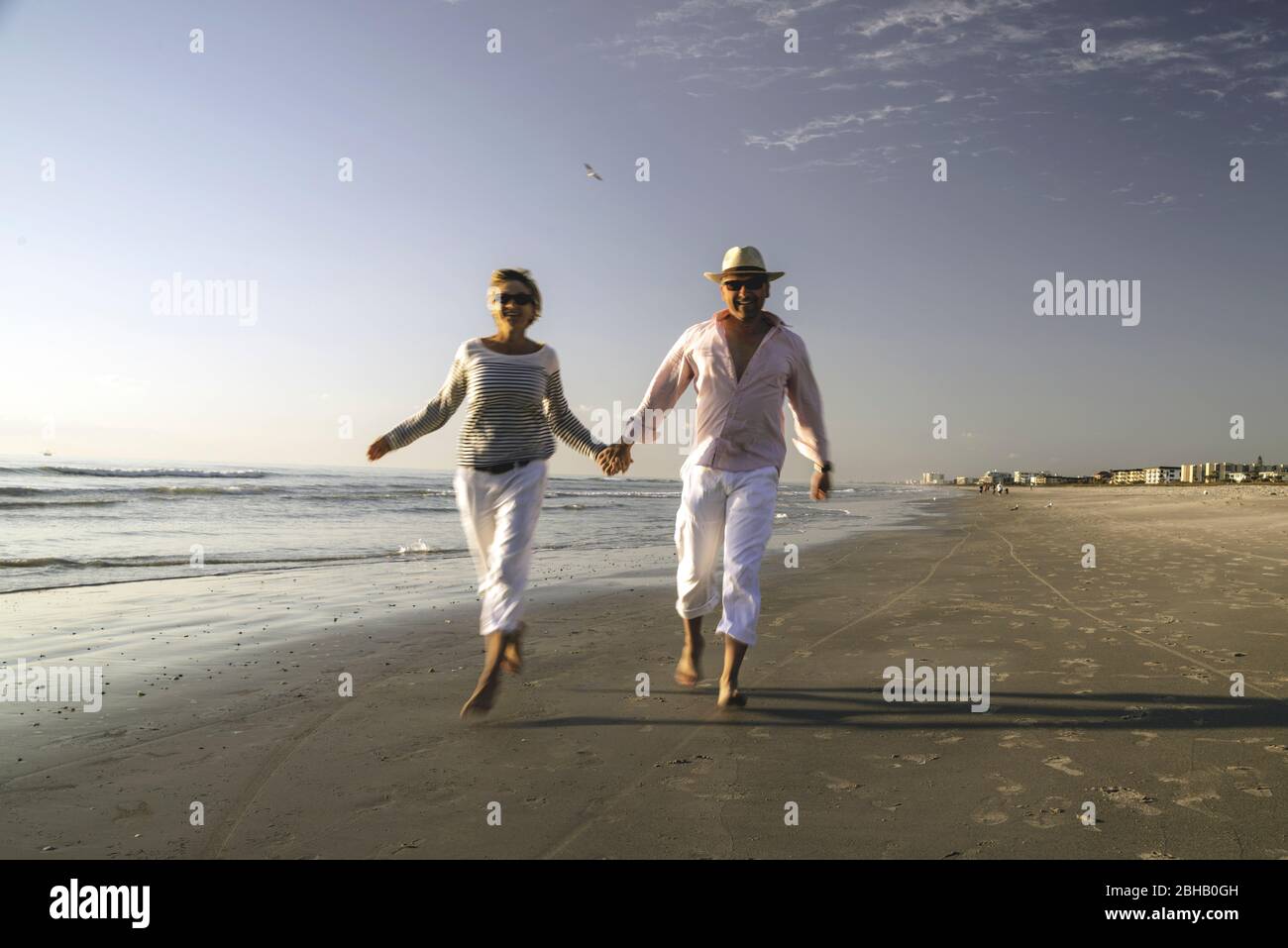 Couple in maritime outfit running over in the surf area of the deserted beach of Daytona Beach and looking friendly in the camera Stock Photo