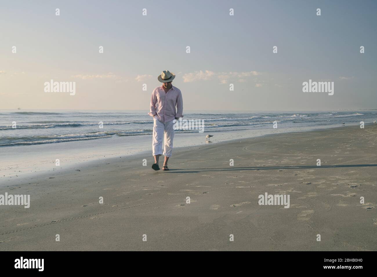 Man with hat and white trousers runs in the surf at the sea, gulls in the background Stock Photo