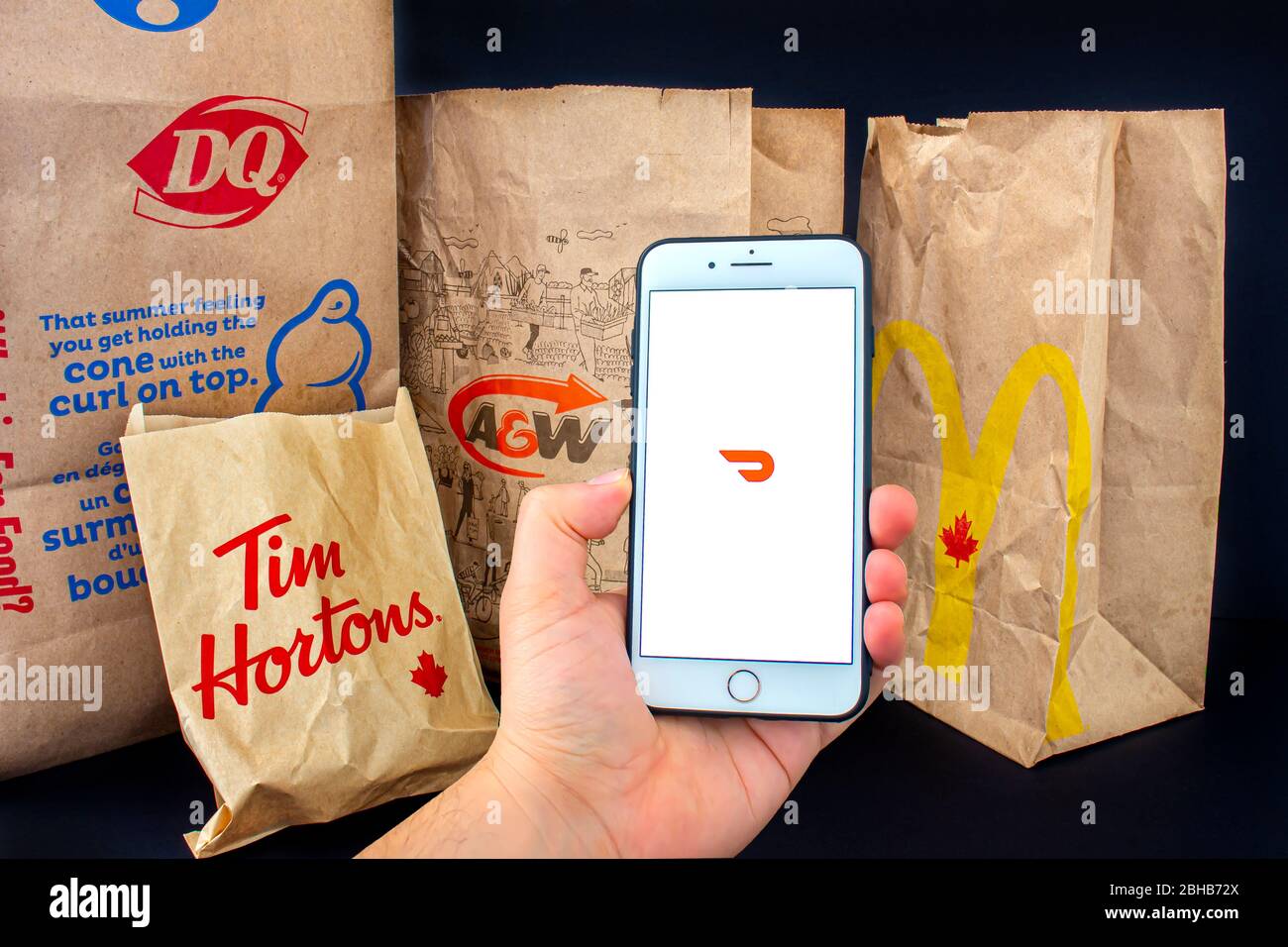 Calgary, Alberta. Canada. April 24, 2020: A person holding an iPhone Plus with the Door Dash application open with delivered food bags from Tim Hourto Stock Photo