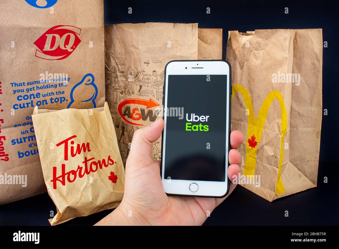 Calgary, Alberta. Canada. April 24, 2020: A person holding an iPhone Plus with the Uber Eats application open with delivered food bags from Tim Hourto Stock Photo