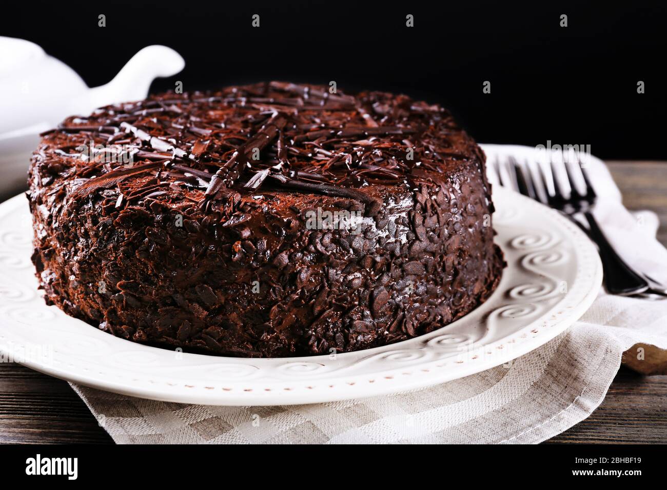 Delicious chocolate cake in plate on wooden table on dark background ...
