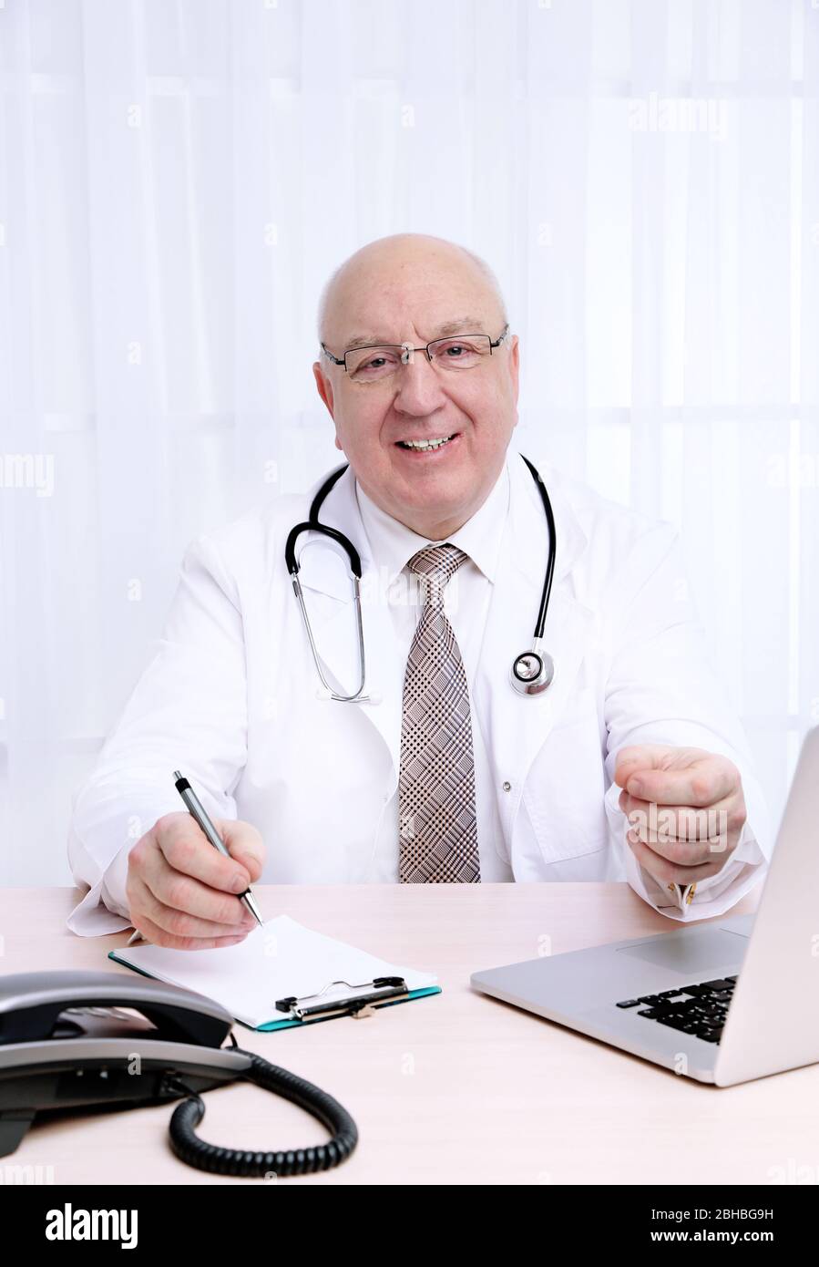 Portrait of professional doctor at table in his office on white curtain ...