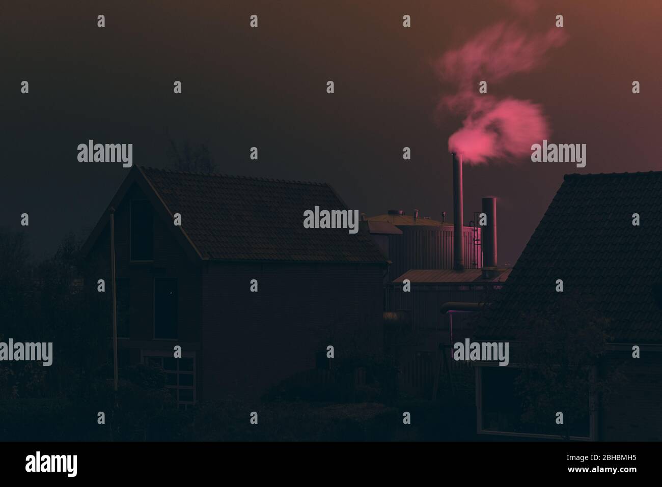 Pink smoke over roofs during night time. Pink Orange color by illumination of greenhouses. Light pollution in The Netherlands. Stock Photo
