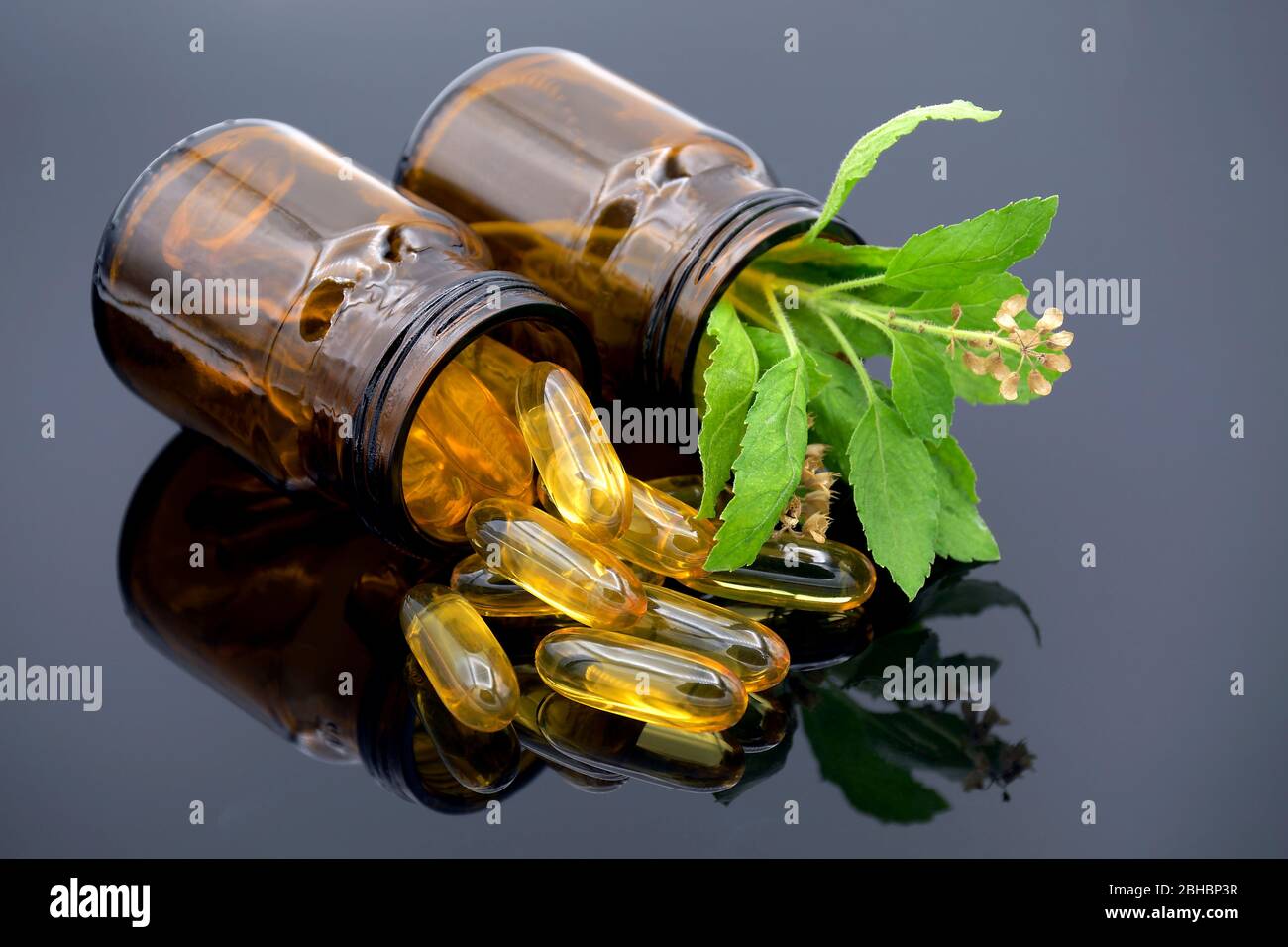 Oil in capsule, amber bottle and fresh herbs on dark background in traditional medicine concept. Stock Photo