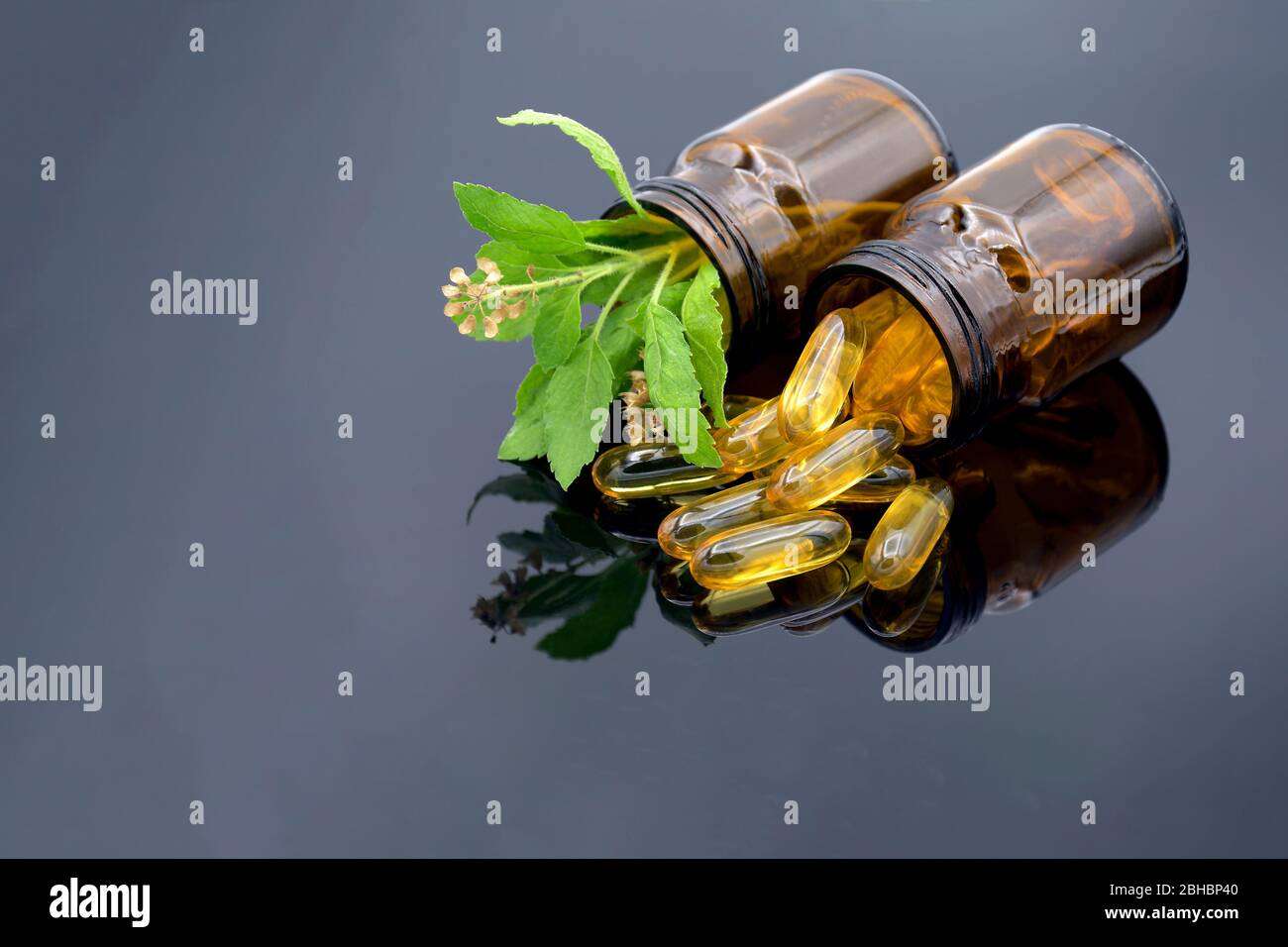 Oil in capsule, amber bottle and fresh herbs on dark background in traditional medicine concept. Stock Photo