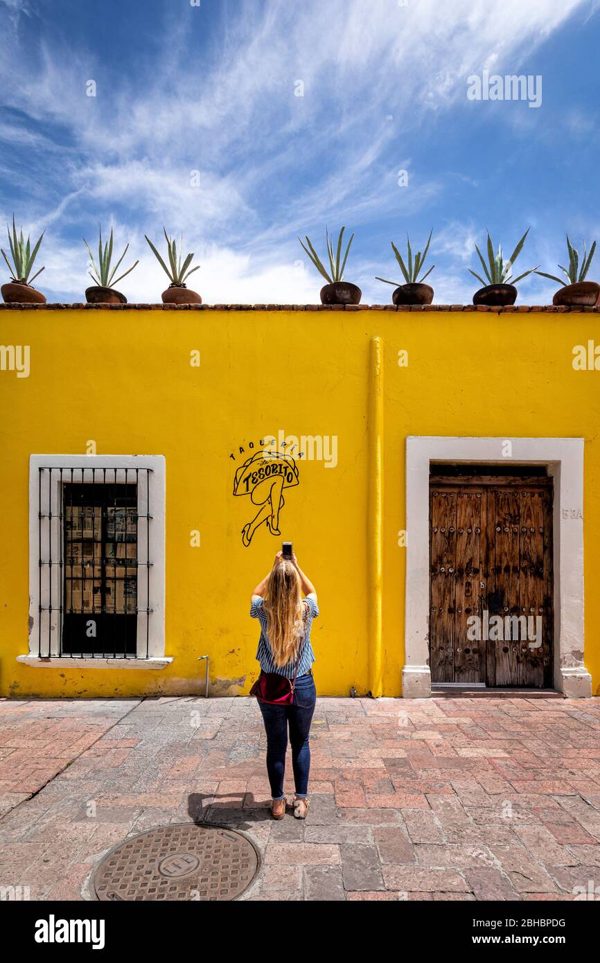 A young blond female photographs a colorful building on the 5 de Mayo pedestrian walkway in downtown Queretaro, Mexico. Stock Photo