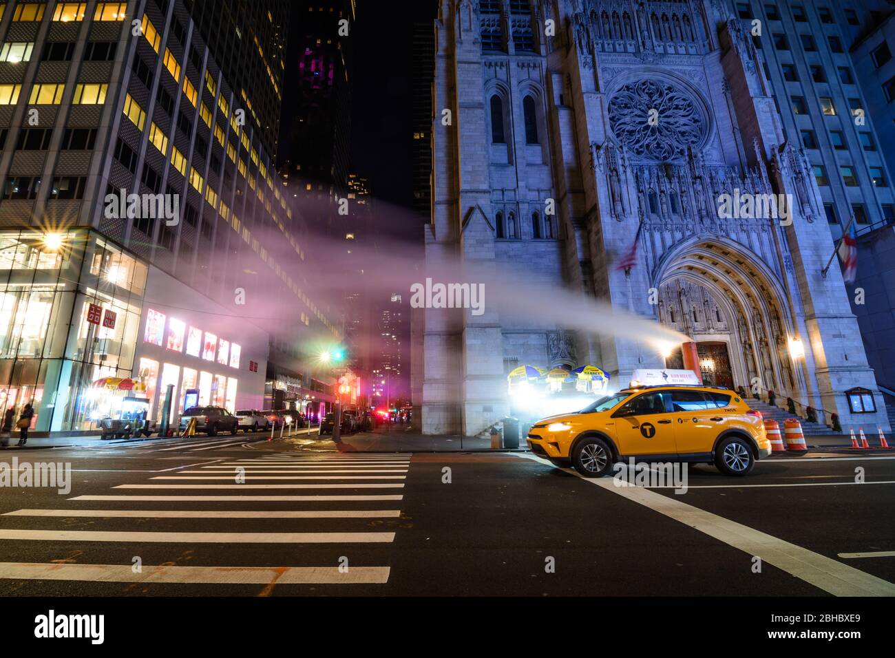 A lone taxi cab at night sits at an intersection in Midtown Manhattan, New York City Stock Photo