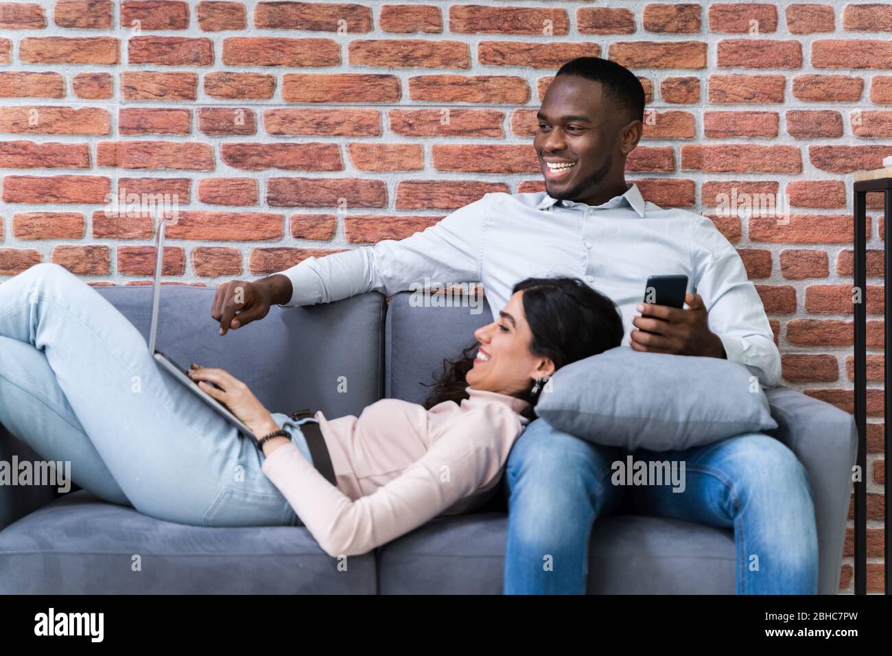 Couple Using Laptops While Relaxing On Sofa At Home Stock Photo