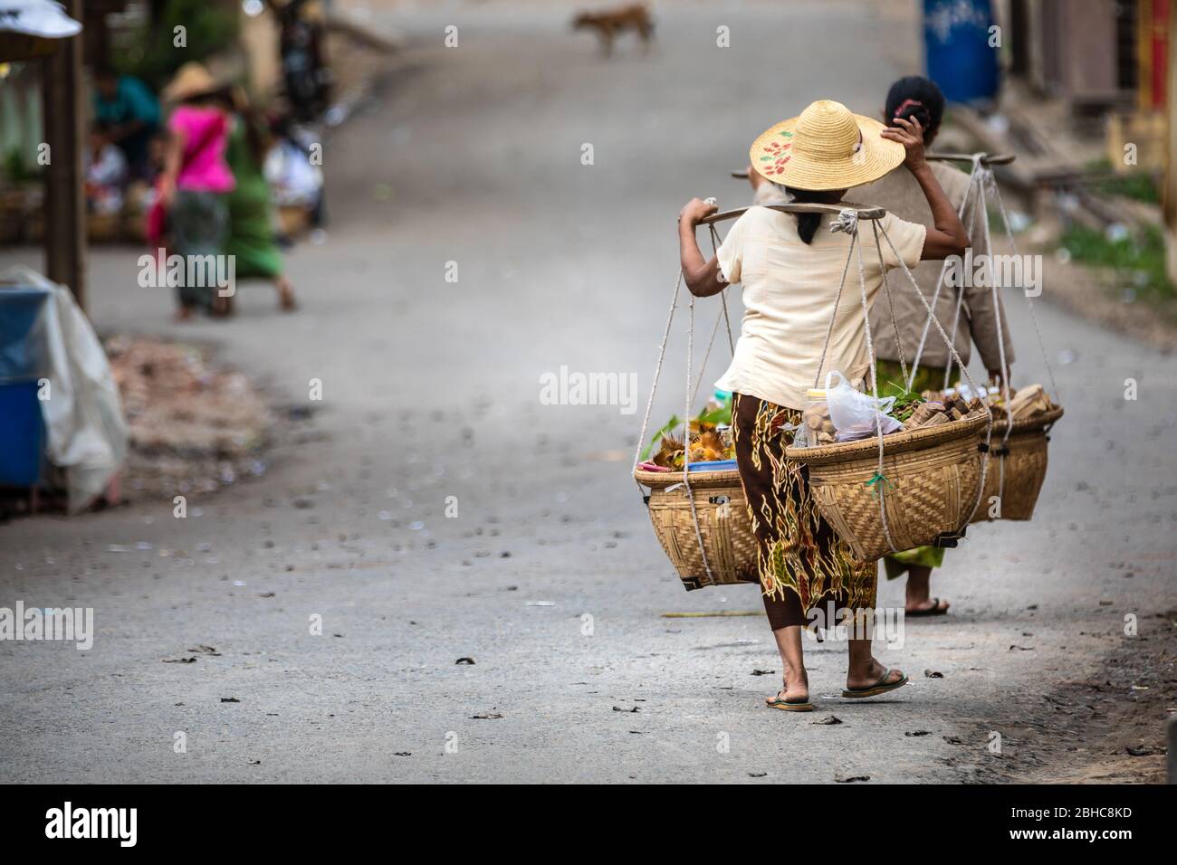 Burmese women who carry food with a typical method. Clothes with characteristic hat of the place. On the street with copy space on the left. Location: Stock Photo