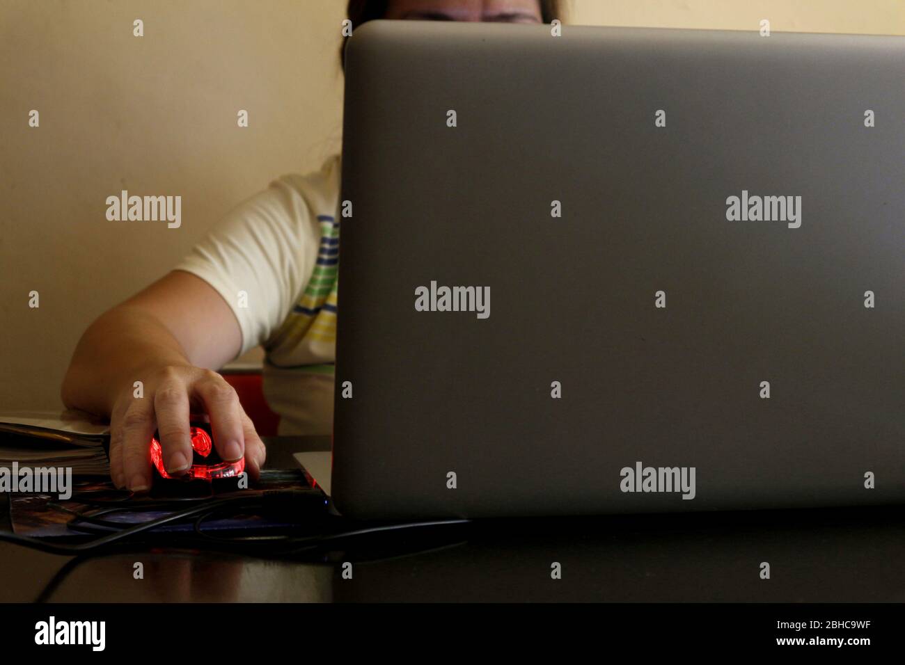 Photo of a Filipino woman's hand holding a computer mouse while working on a laptop computer at
