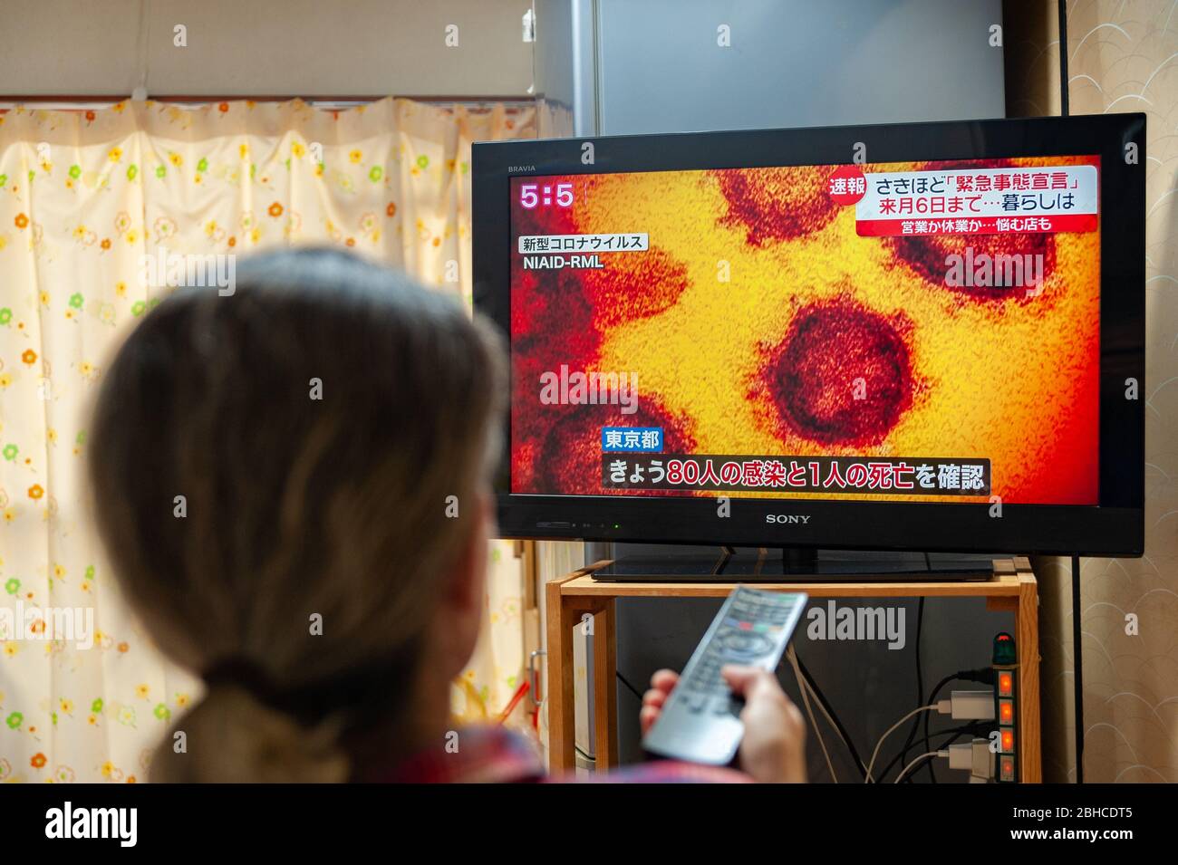 Fuji City, Shizuoka, Japan - April 7, 2020: A woman watches a newscast on Japanese TV about the spread of the coronavirus (COVID-19) in Japan. Stock Photo