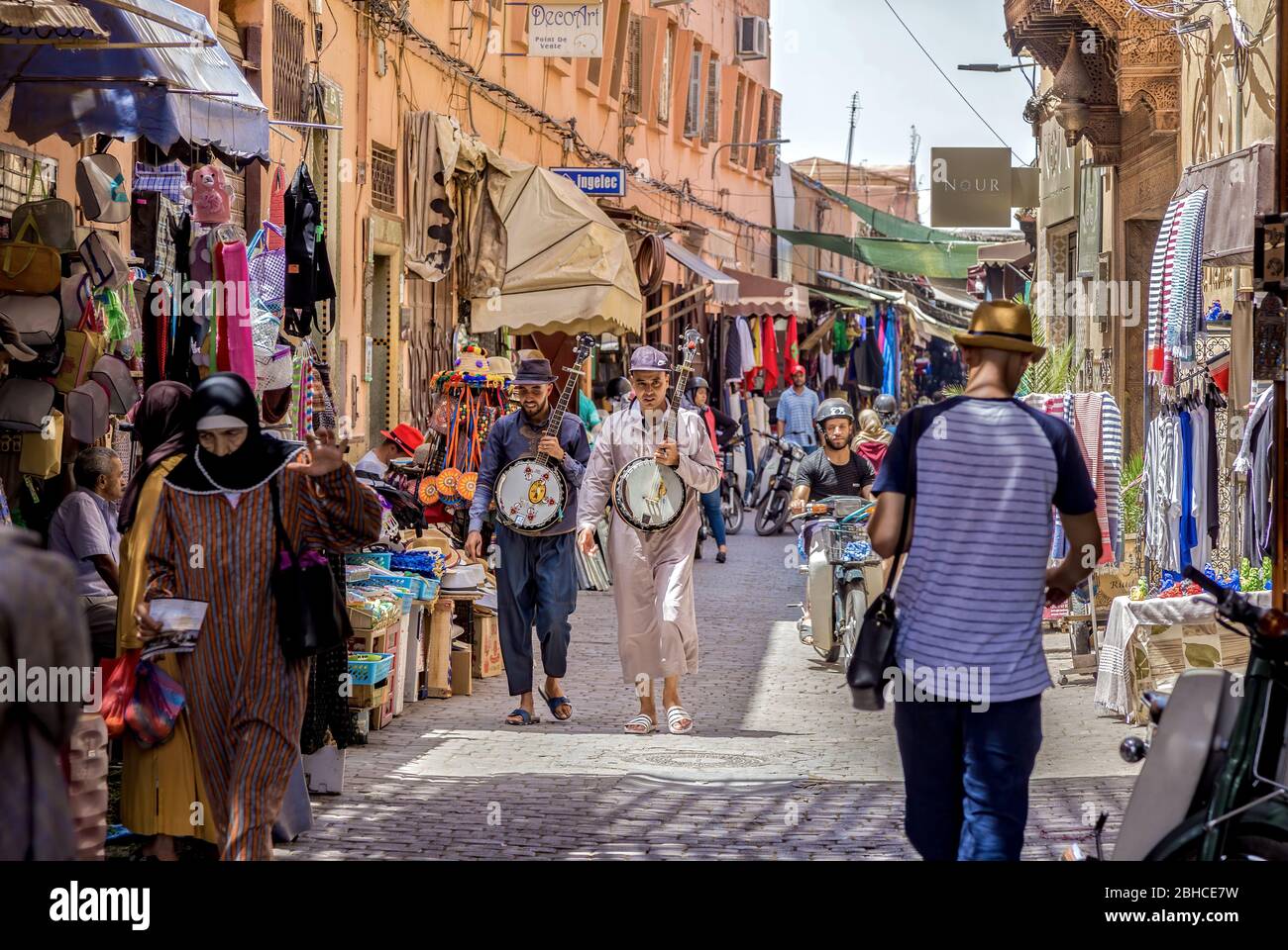 Typical street view of Marrakesh Medina Bazaar in Morocco. Crowded with hanging goods. Street musicians walk in the middle of the street Stock Photo