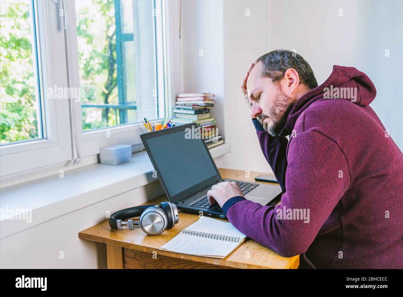 Man working from home office. Adult bearded man concentrated, working online from home on computer laptop behind vintage desk Stock Photo