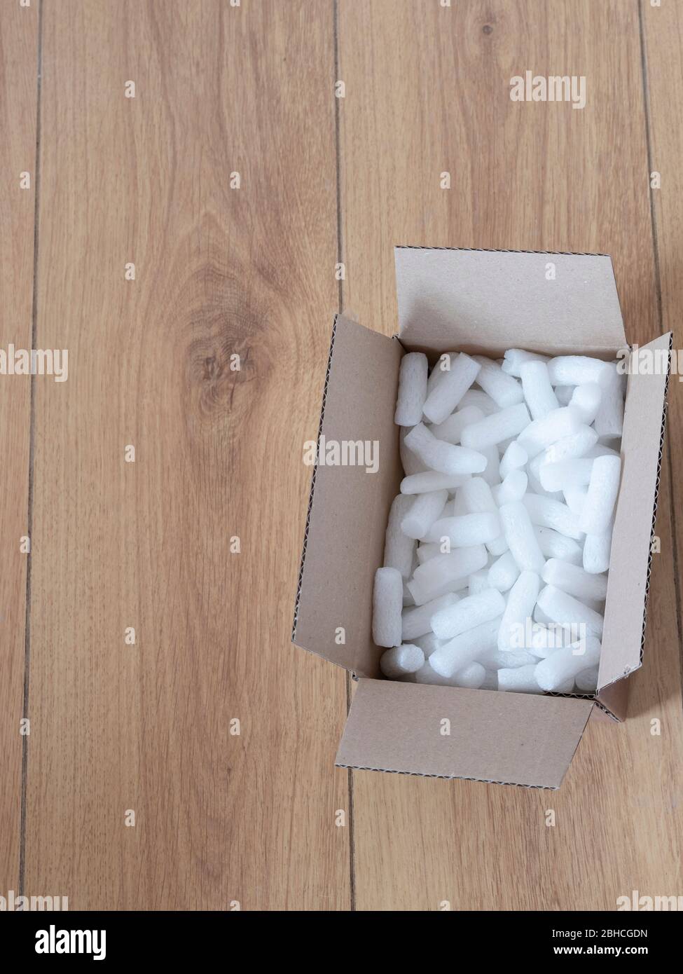 A cardboard box with packing foam pellets top view, on wooden floor Stock Photo