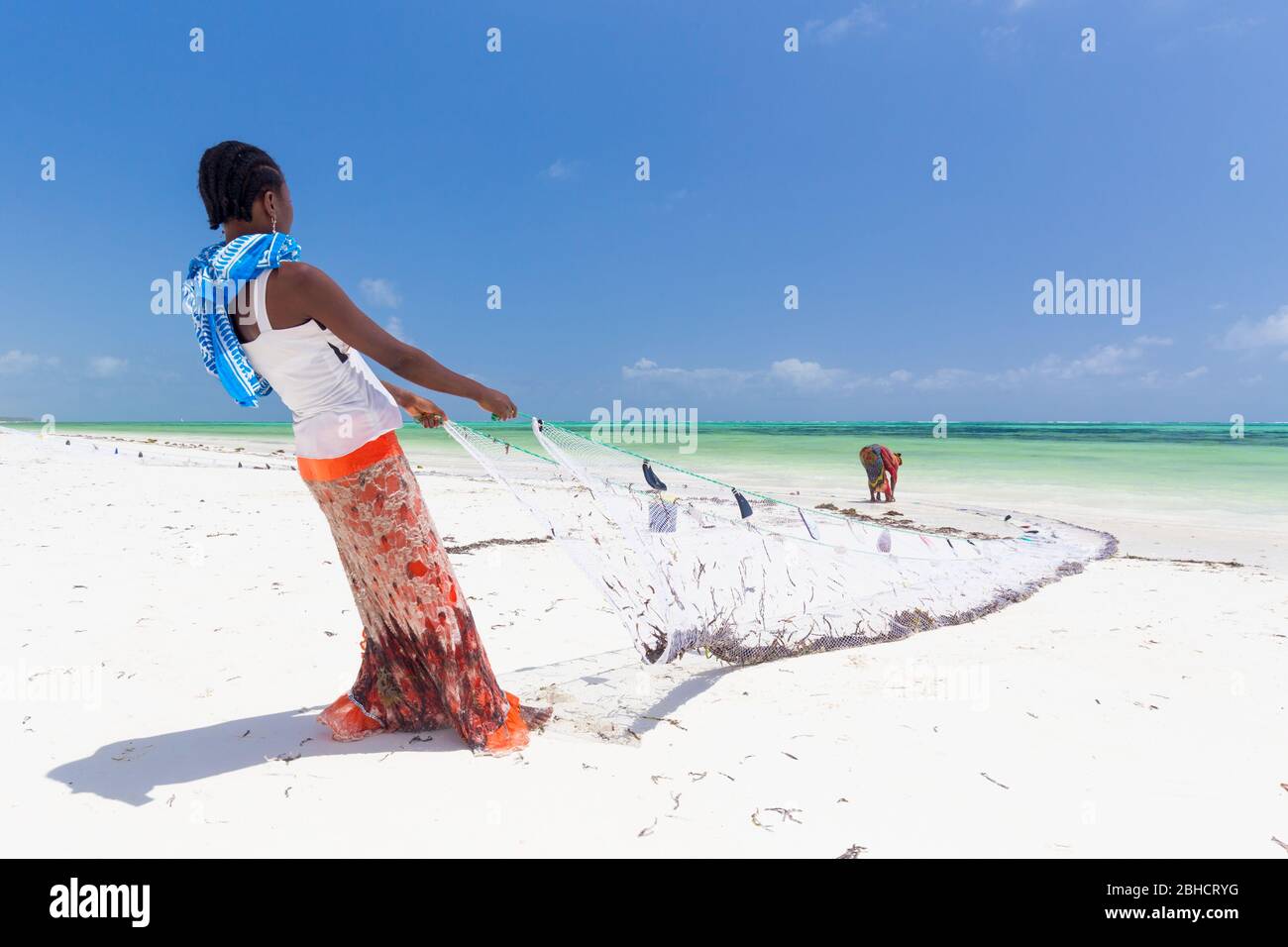 Traditional african local rural fishing on Paje beach, Zanzibar, Tanzania. Traditionally dressed local woman pulling fishing net, catching small fish. Stock Photo