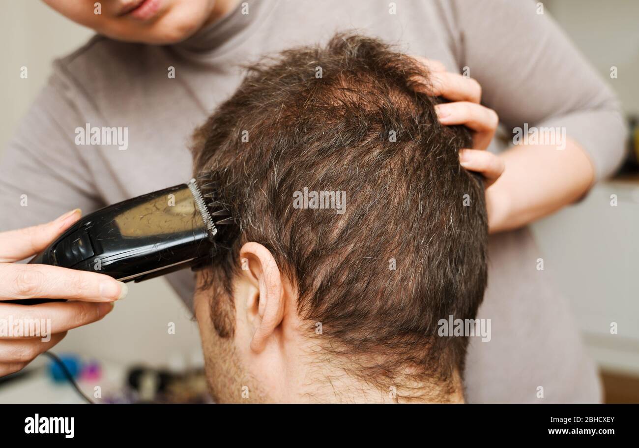 Woman is doing haircut with hair trimmer to man at home Stock