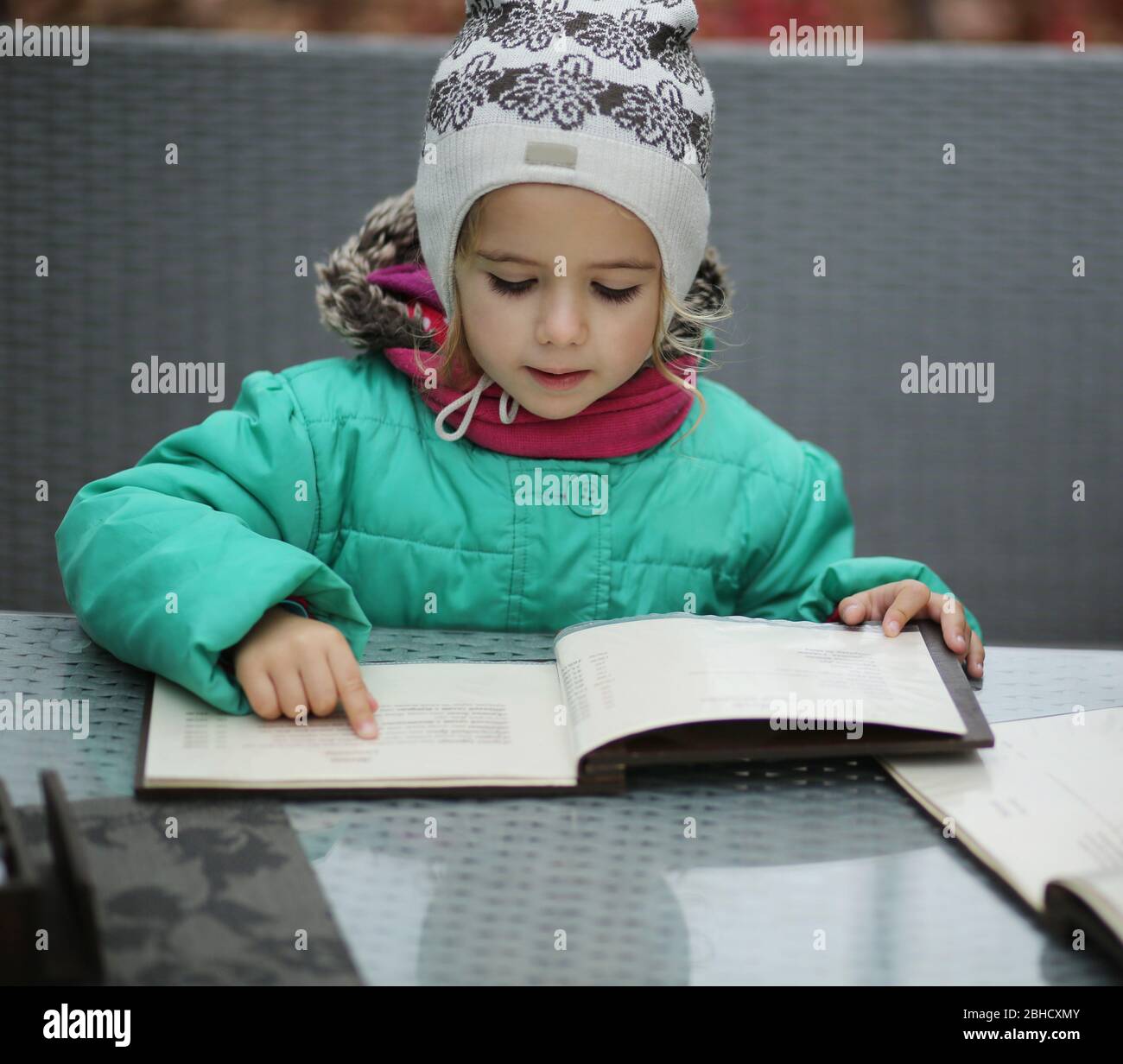Three year old girl reading a menu in the outdoor cafe terrace Stock Photo