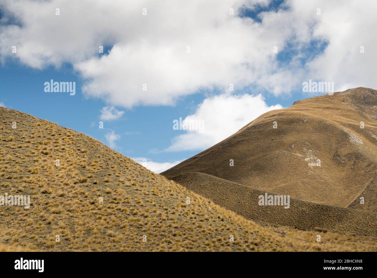 Cropped in abstract view of monchrome treeless brown undulating hills with white cloud and blue sky above Stock Photo