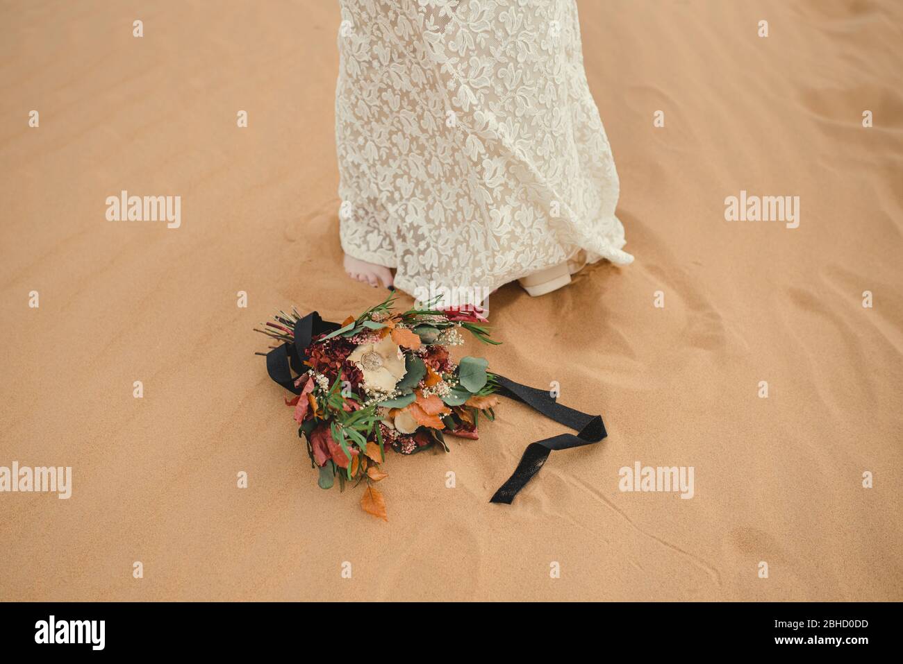 bridal bouquet lying on the sand next to the bride's feet. Stock Photo