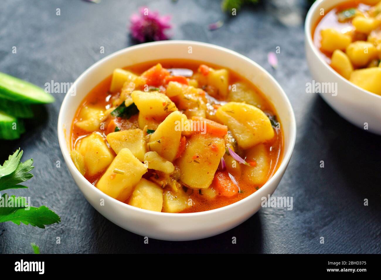 Vegetable stew in a white bowl. Photo food. Stew with potatoes and carrots on a dark concrete background. Healthy vegetarian food. Stock Photo