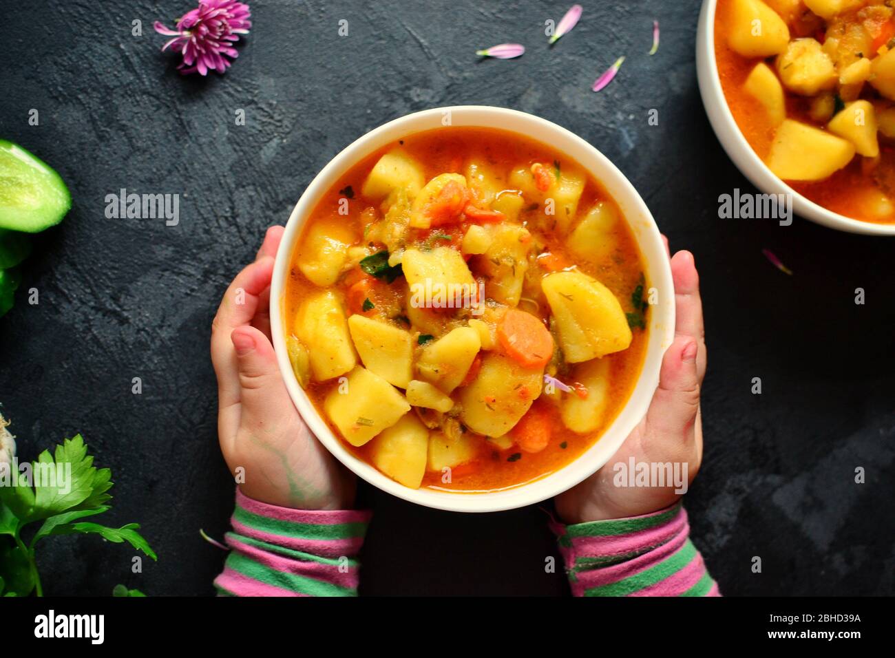 Photo of food on a dark background. Children's hands and food. The child holds hands a bowl with vegetable stew. Baby is having lunch. Food on a Stock Photo