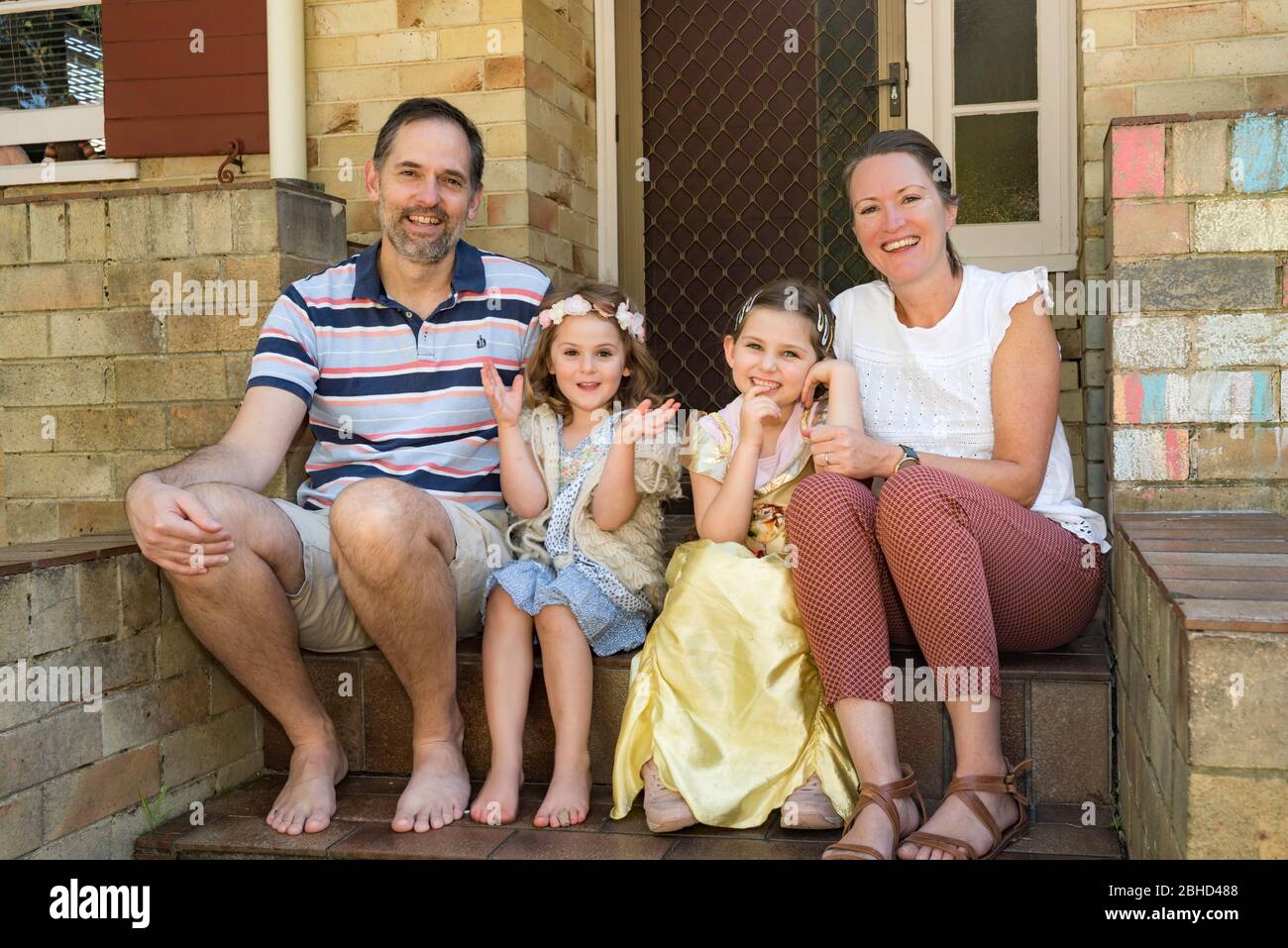 A smiling Zimbabwean family living in Australia sit at the front steps of their Sydney home during the Covid-19 epidemic. Stock Photo