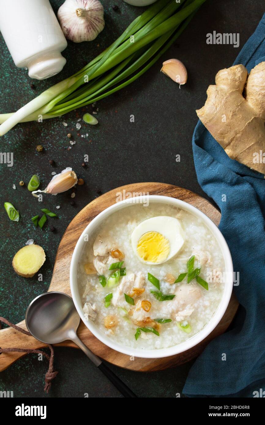 Arroz Caldo Soup. Hot soup with ginger chicken rice and garlic in a bowl on a dark countertop. Top view flat lay background. Stock Photo