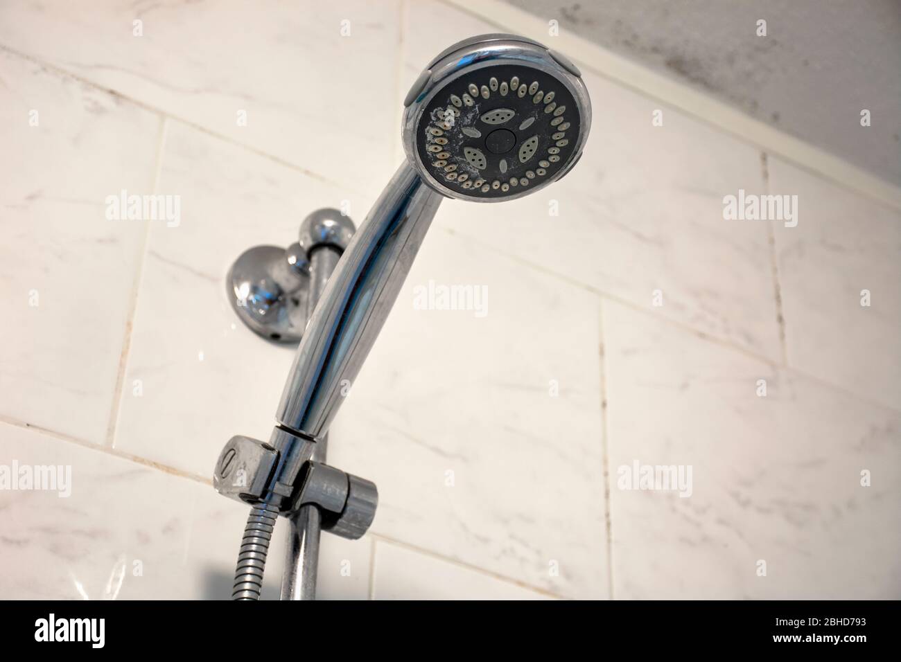 Dirty chrome shower head with limescale that should be cleaned and mold on tiles and ceiling. Calcified shower due to hard water. Calcium mineral buil Stock Photo