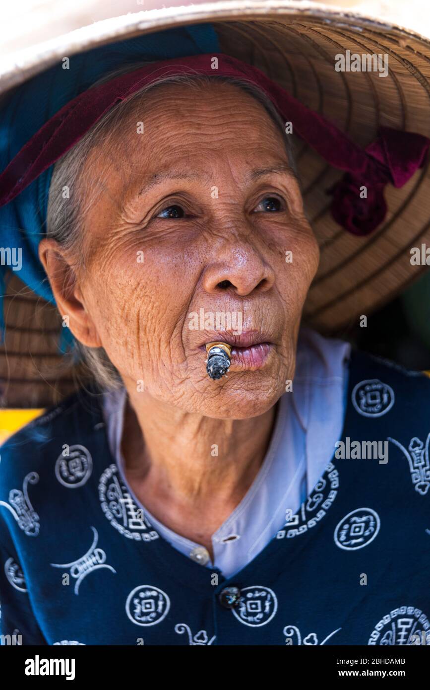 Hoi An, Vietnam, January 20, 2020 - old wrinkled vietnamese lady smoking and looking at camera Stock Photo